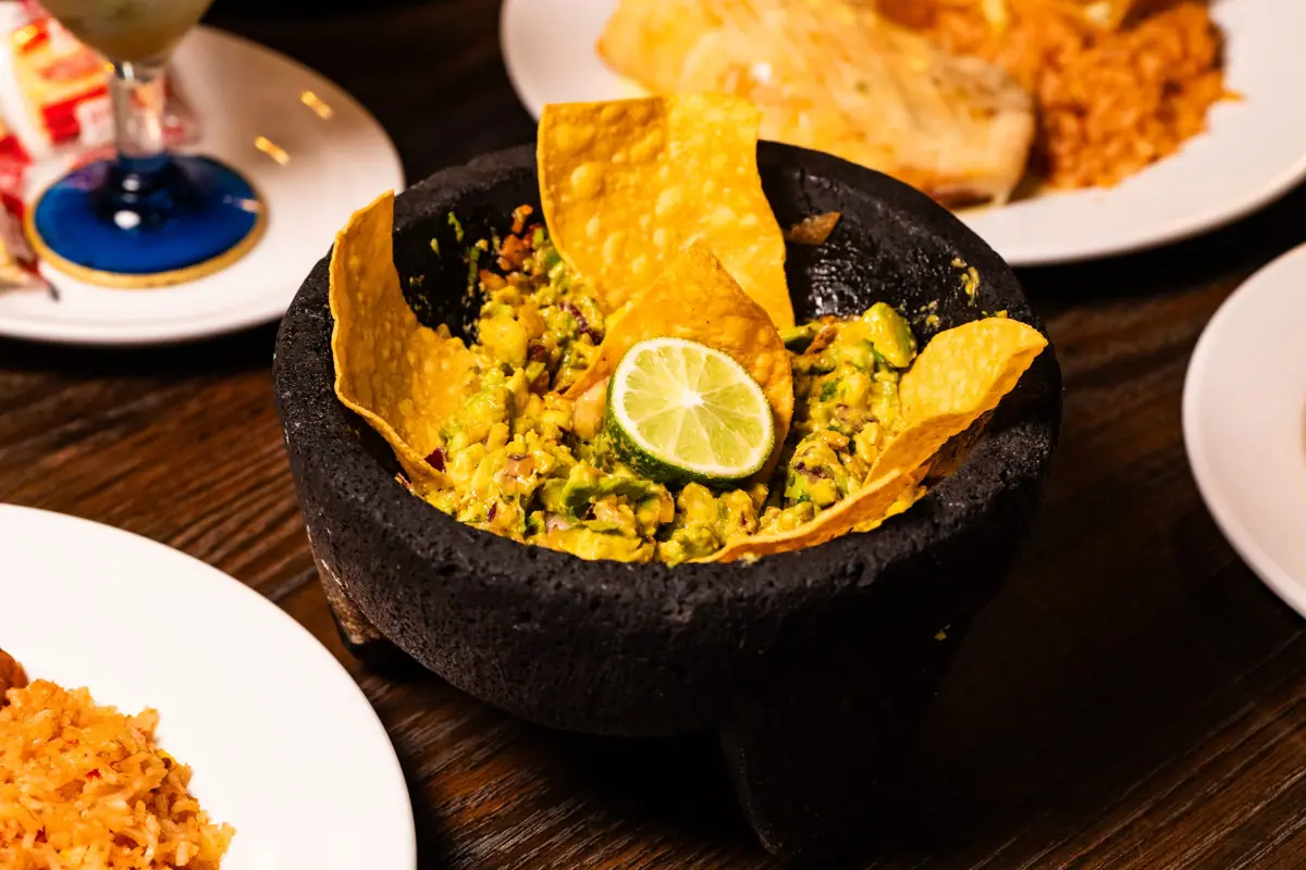 Guacamole Mexicano in a molcajete with tortilla chips and lime