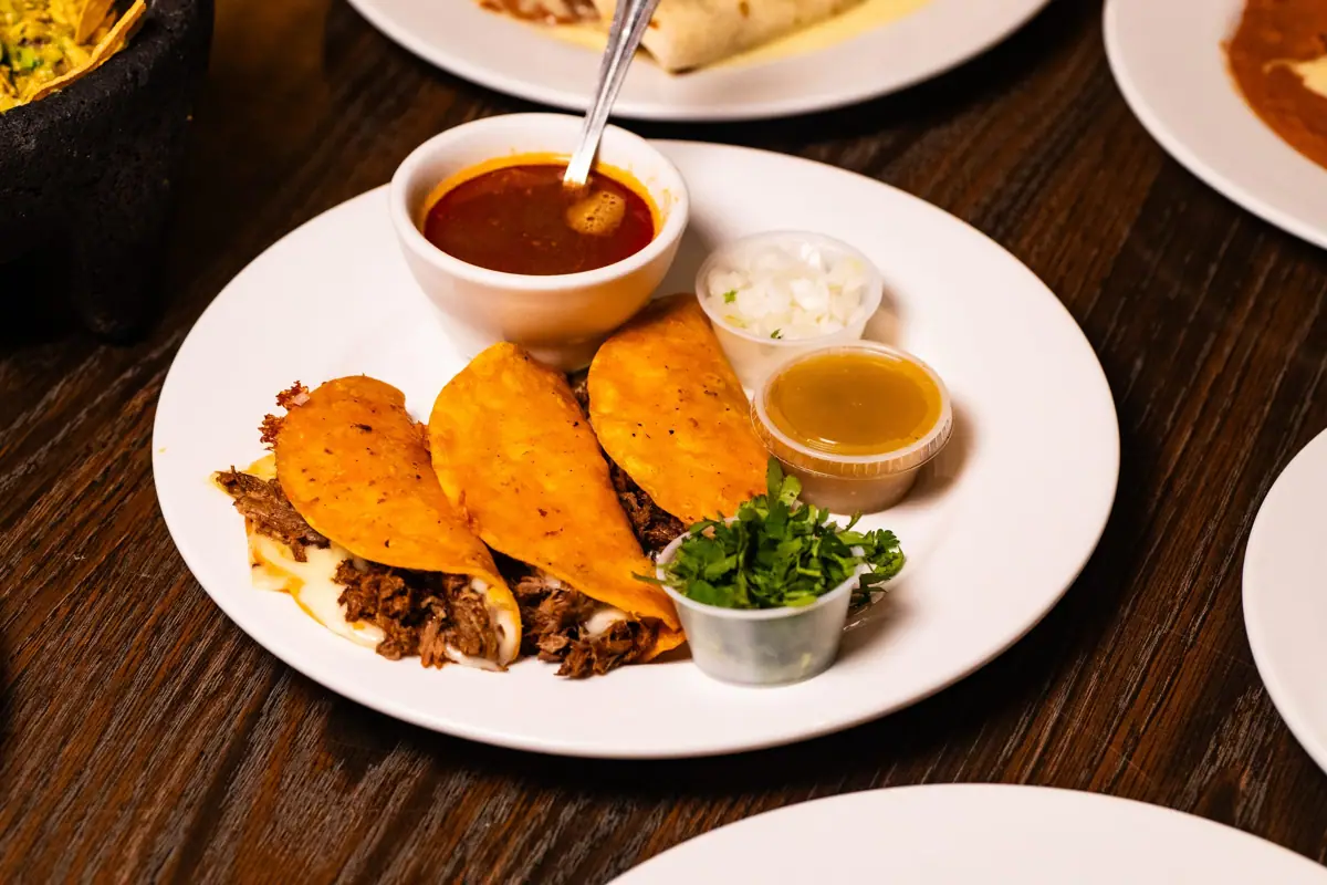 Quesabirria with a cup of birria consommé, cilantro and onions